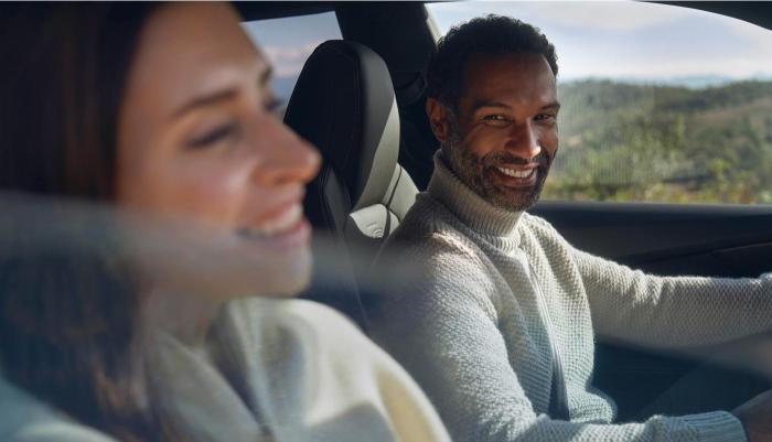 Blick durch das Beifahrerfenster in ein Audi Modells. Ein Mann und eine Frau unterhalten sich gut gelaunt während der Fahrt.