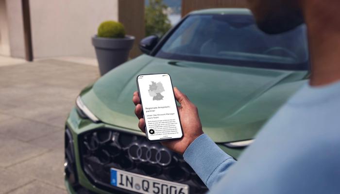 Eine männliche Person mit Smartphone vor einem Audi Q5 Sportback.