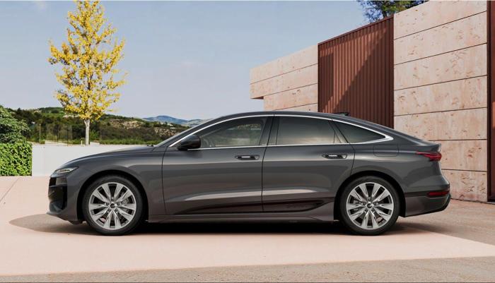 Der Audi A6 Sportback e-tron vor einem modernen Gebäude in mediterraner Landschaft. Zu sehen ist die im 180-Grad-Winkel aufgenommene Fahrerseite.