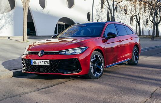 Der Passat R-Line in Chilirot Metallic steht am Straßenrand, dahinter eine wei0e Häuserzeile