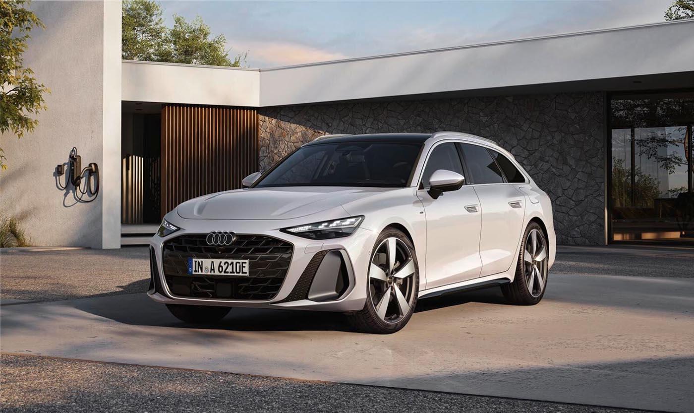 Eine Audi A6 Avant e-hybrid in Gletscherweiß Metallic vor einem modernen Wohngebäude. Zu sehen sind die Fahrzeugfront und die Fahrerseite.