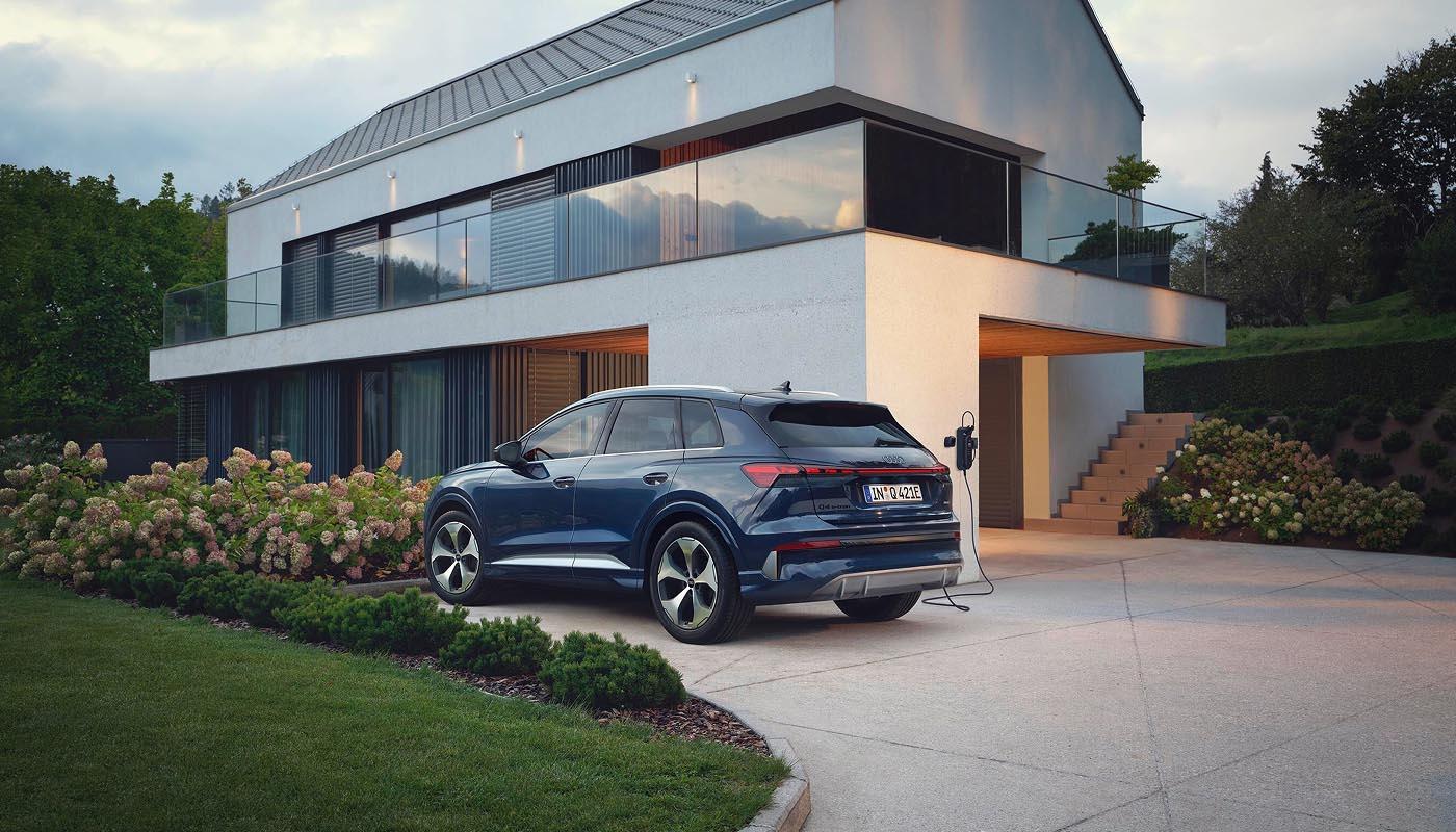 Ein Audi Q4 e-tron SUV in Plasmablau Metallic parkt vor einem Wohngebäude in moderner, klarer Architektur.