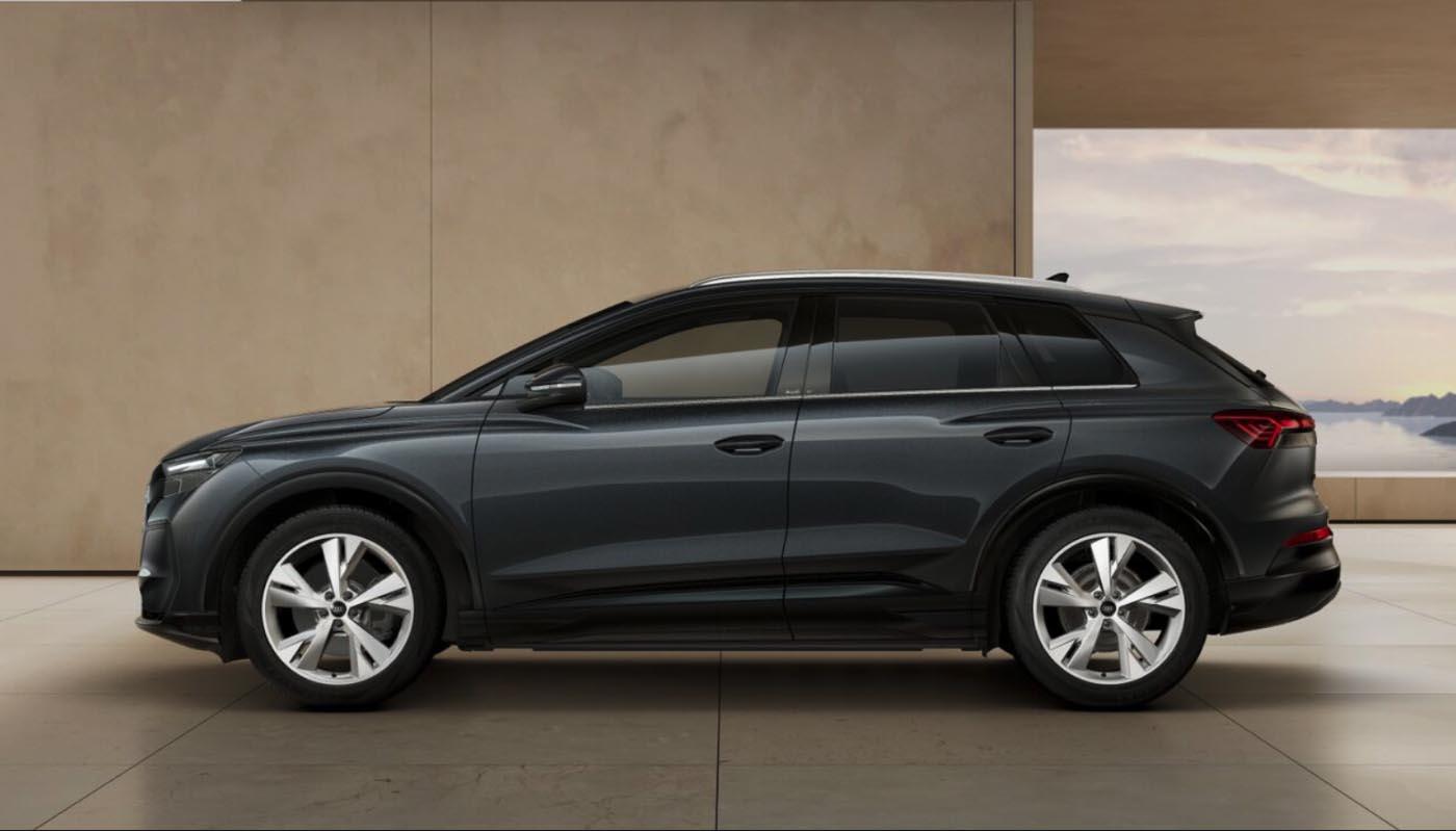 Seitenansicht des Audi Q4 SUV e-tron in Tamboragrau Metallic vor den klaren Flächen einer modernen Gebäudefassade. 